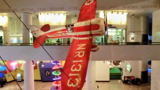 シカゴ科学産業博物館に展示されたレトロな赤い飛行機。100万マイルへのばかげた挑戦を象徴するようなイメージ。